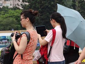 二位游客，一位用ipad，一位用相机，将展示的法轮功真相图片一张张拍下来。