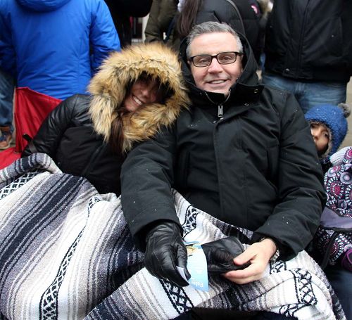图10：多伦多的Paul和妻子裹着被子在看游行，他说：“天国乐团的演奏非常震撼人心，令我感慨的是这么冷的天他们还能吹得这么好听，在给在寒冷中的我们带来温暖。”