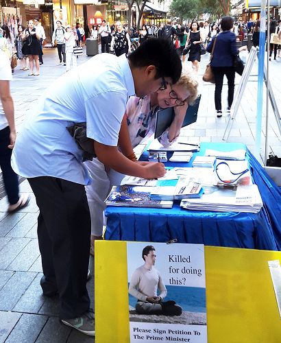 图5：门多萨先生（Christopti Mendoza）在真相摊位前在给澳洲总理的明信片上签名