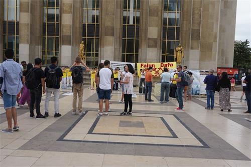 '图3：巴黎人权广场上，过往游客认真阅读法轮功真相展板，观看法轮功学员炼功。'