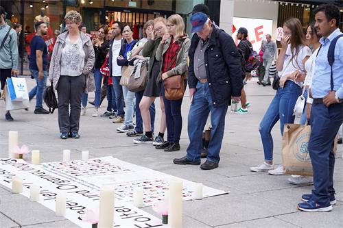 '图5：在法兰克福市中心，法轮功学员举行烛光夜悼活动，路人驻足认真阅读揭露迫害的信息。'