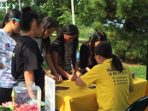 '图2：很多亚裔年轻人围着法轮功学员学做纸折莲花'