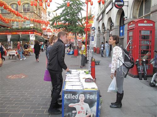 '图9：二零二零年八月十六日，在伦敦唐人街，英国女演员爱琳（Eileen Von Skopnik）看到两位青年走近法轮功信息台，她走上前去鼓励他们签名支持法轮功反迫害'