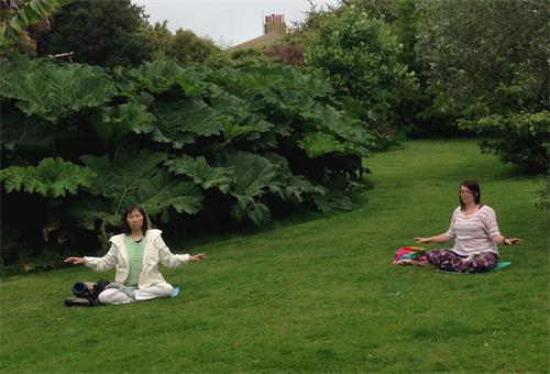 '图2：二零二零年六月二十三日，英国法轮功学员罗斯（Rose，右）与英国日裔法轮功学员鹤田缘（Yukari）在茂拉博花园的草地上炼功打坐'