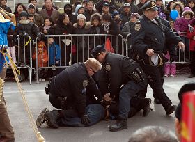右图：纽约法拉盛新年游行活动中，一华裔男子从观众群中冲到法轮功队伍的前面，拉扯横幅并折断横杆。三个警察立即冲上去将其制服并逮捕。