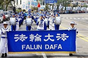 二零一零年十月在韩国仁川的一个市民节日游行中，金先生手持指挥棒引领由法轮功学员组成的军乐队。