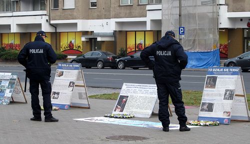 图6：华沙中使馆门前，执勤警察观看法轮功真相展板