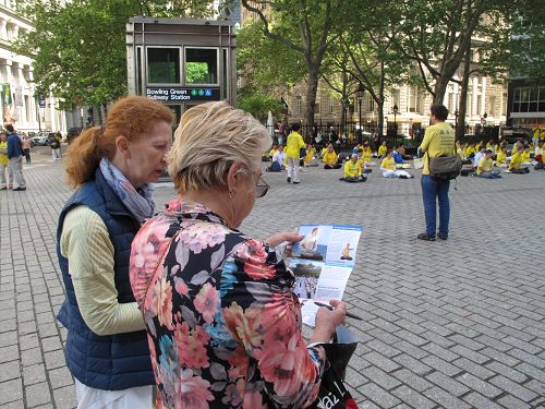 图6：来自东欧的米丽娜女士（右）在纽约美国国家图书馆前一边观看法轮功学员集体炼功，一边阅读真相传单。