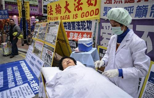'图：二零一三年一月十二日，法轮功学员在香港的一个购物区模拟中共强摘器官暴行。他们说他们的同修受到酷刑迫害，并被强摘器官。'