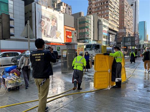 '图1：二零二一年一月二十九日，香港食环署清洁工用水龙头、借故清洗街道，欲阻止法轮功学员开设真相点。'