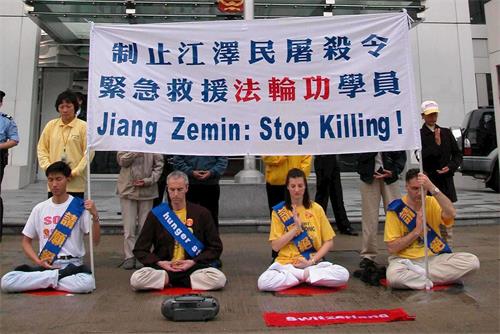 '图2：二零零二年三月十四日，四名瑞士和十二名香港的法轮功学员在西区中联办前绝食静坐，抗议中共迫害残杀大陆法轮功学员，遭警方武力粗暴抬走。'
